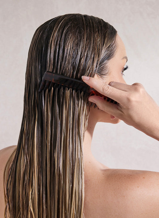 Woman combing wet hair with wide-tooth comb using hair detangler for smooth and tangle-free strands.