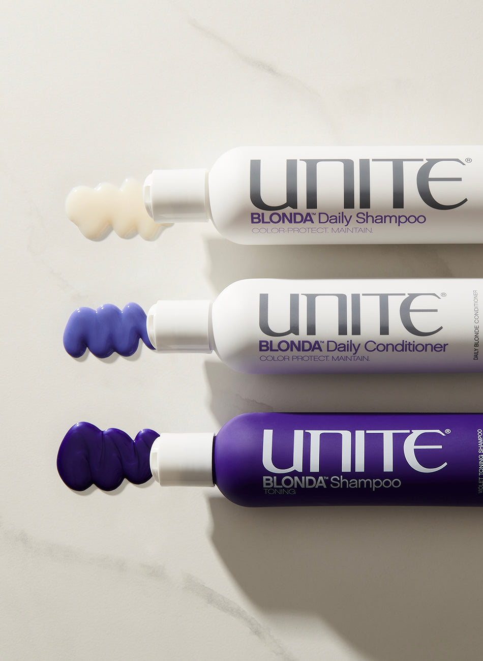 Purple conditioner and shampoo bottles with product swatches on a light surface.