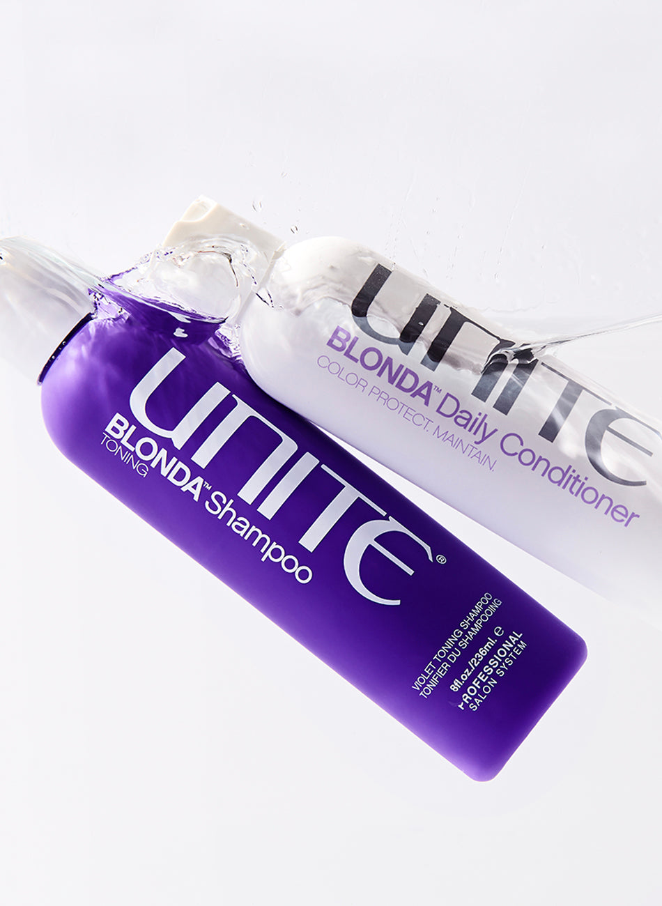 Bottles of violet shampoo and purple conditioner partially submerged in water.