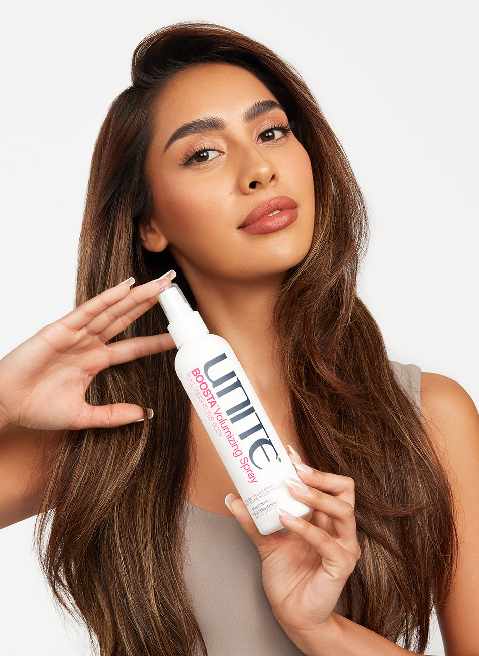 Woman with voluminous brown hair holding a bottle of volumizing spray for styling.