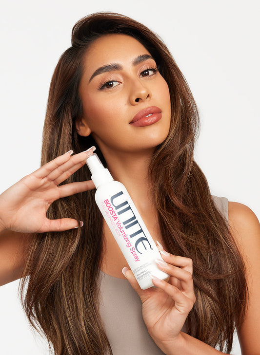 Woman with voluminous brown hair holding a bottle of volumizing spray for styling.