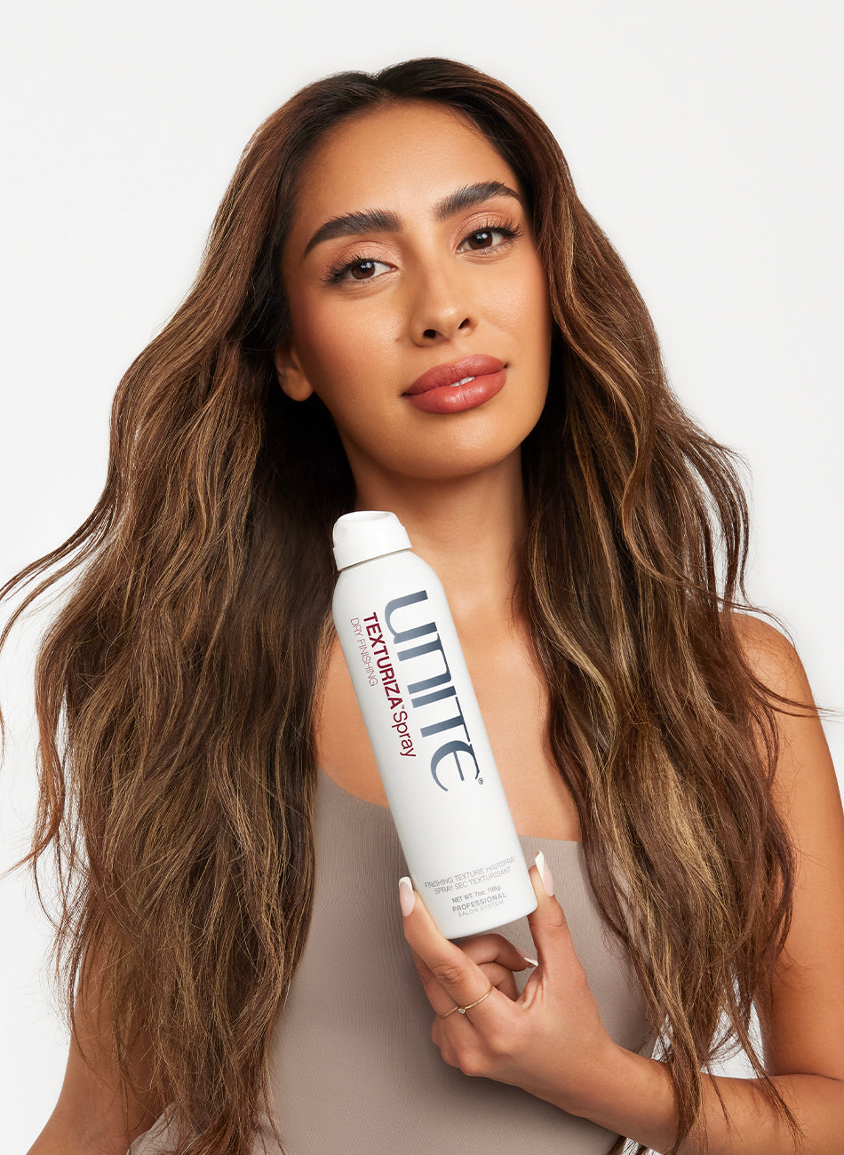 Woman with voluminous wavy hair holding a can of texturizing spray hair product.